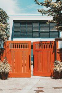 Stylish wooden gates open to reveal a modern villa facade, surrounded by lush tropical plants.